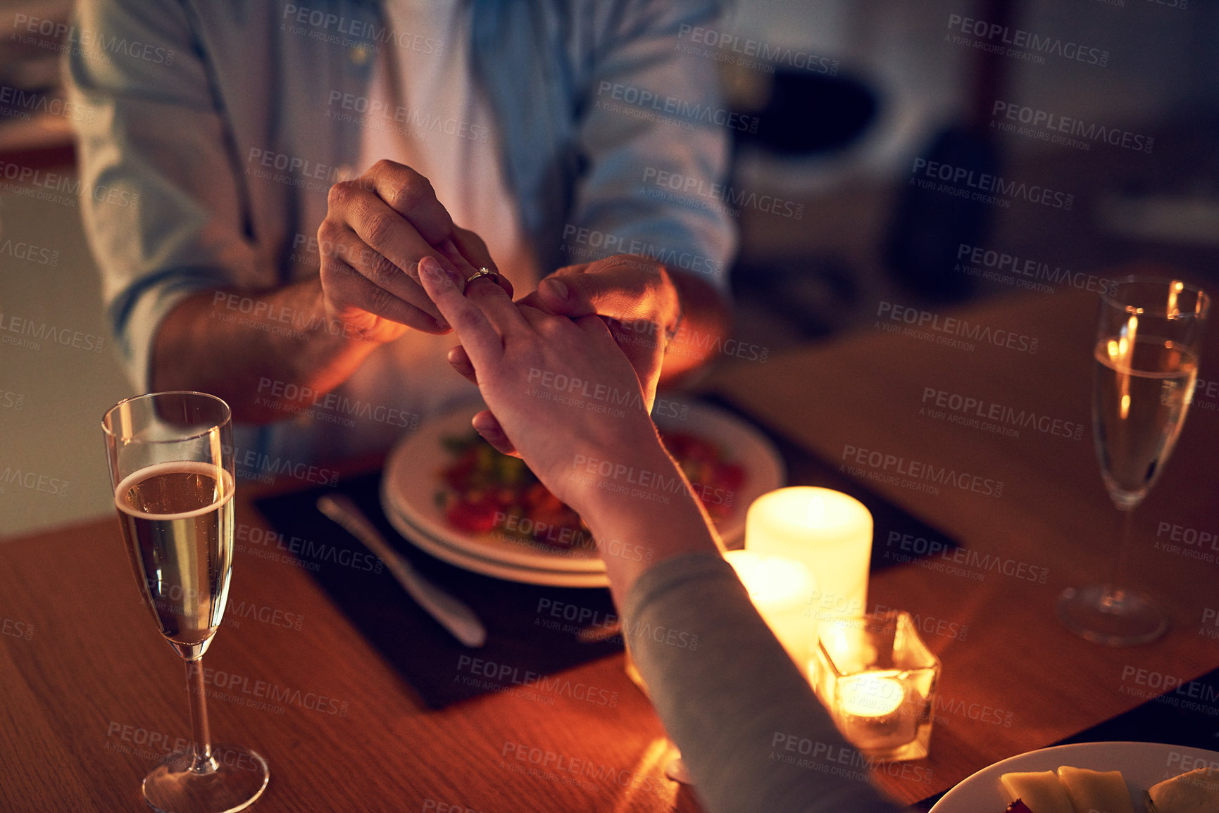 Buy stock photo Cropped shot of an unrecognizable man proposing to his wife over a candle lit dinner at night