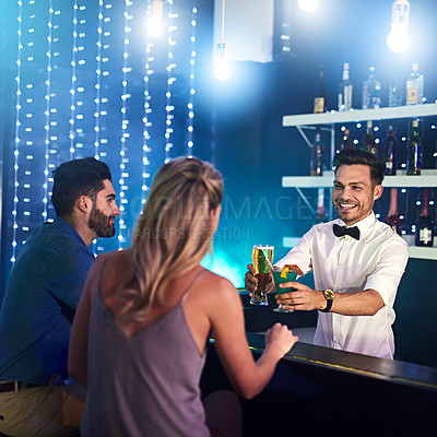 Buy stock photo Shot of a happy bartender serving drinks to a couple in a nightclub