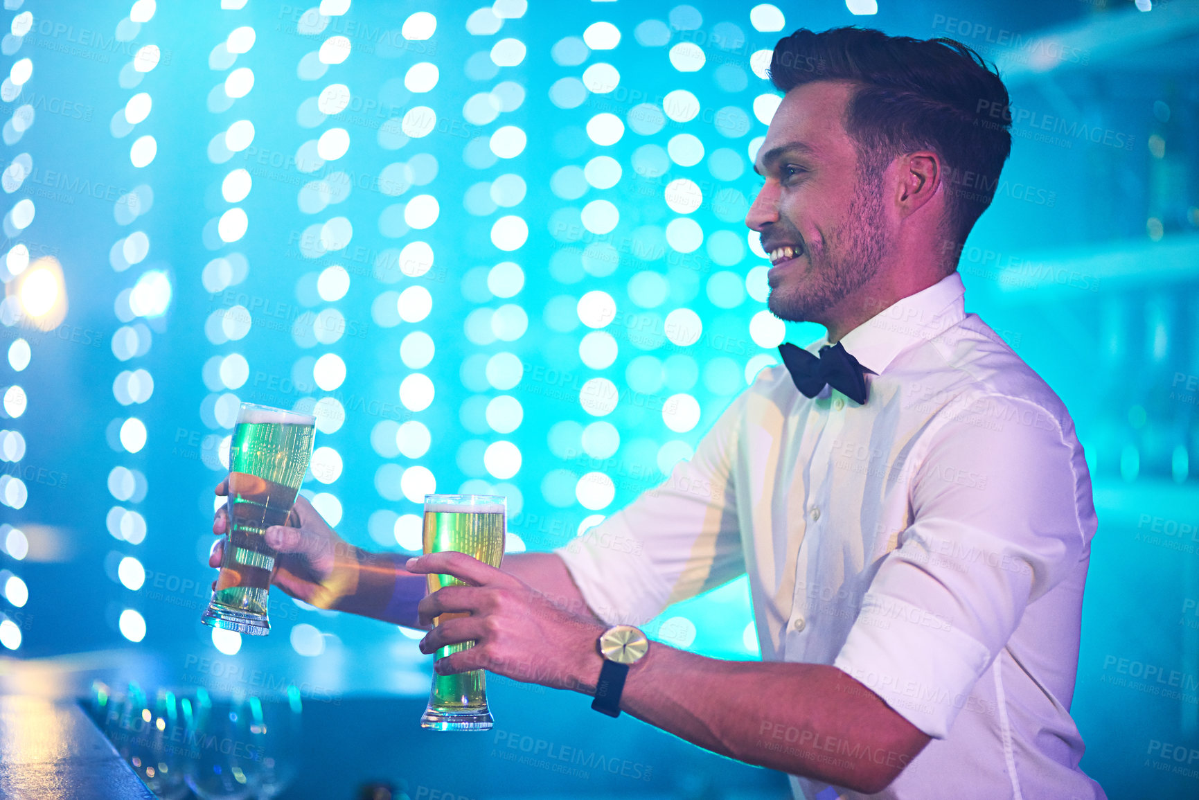 Buy stock photo Shot of a happy bartender serving two glasses of beer at a bar