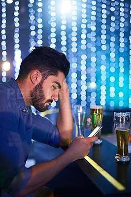 Buy stock photo Shot of a young man looking upset while using his phone at a bar