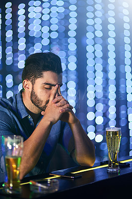Buy stock photo Shot of a young man looking stressed out while having drinks at a bar alone