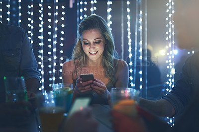 Buy stock photo Shot of a young woman texting on her smartphone while sitting in a crowded nightclub