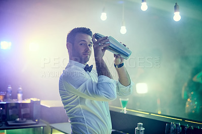 Buy stock photo Portrait of a handsome young barman mixing a cocktail in a nightclub