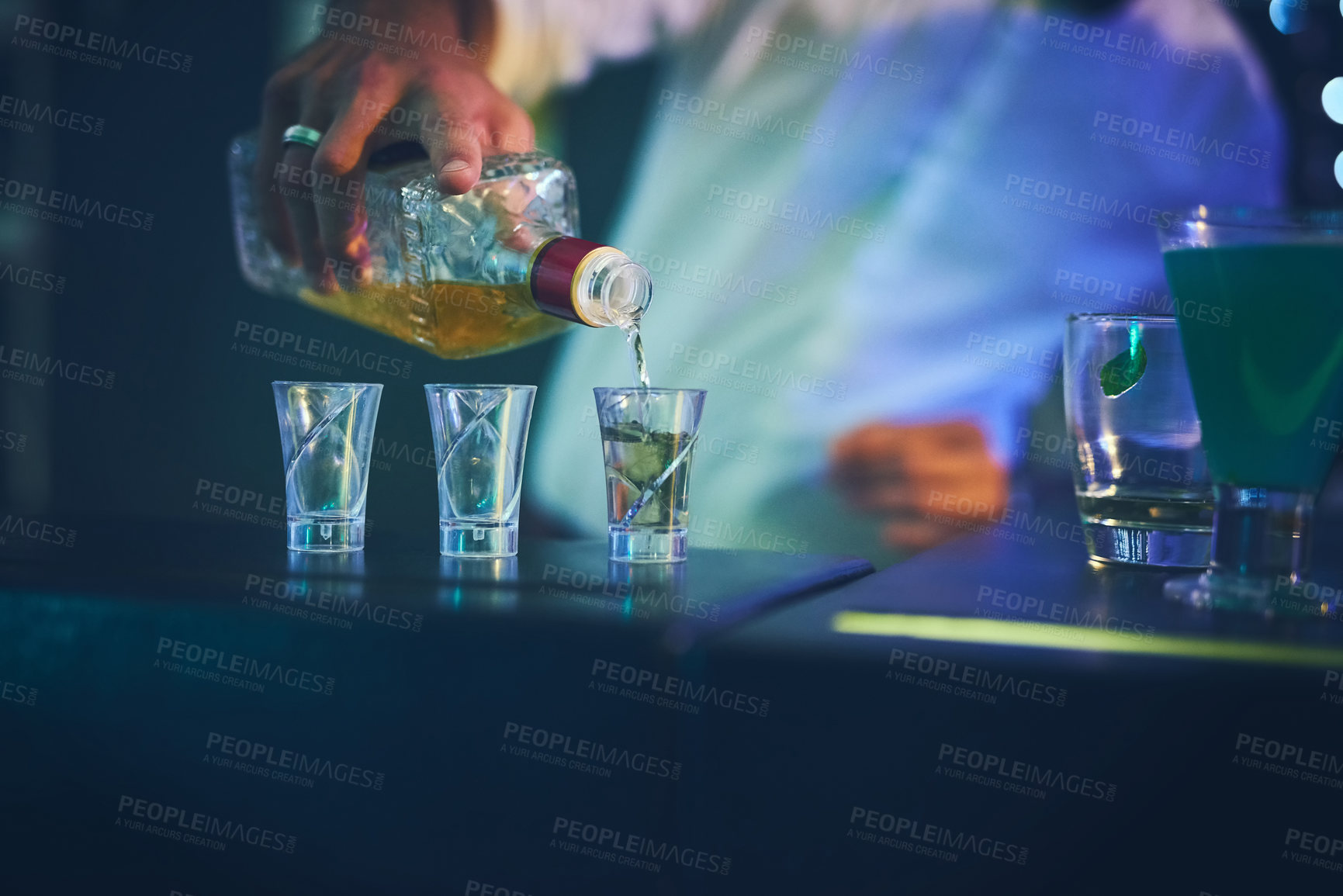 Buy stock photo Barman, bottle and pour in shot glasses at night club for service, order and counter server with hospitality. Bartender, employee and hand with prepare spirits in glass at social event and happy hour