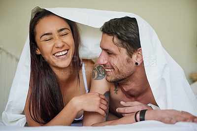 Buy stock photo Shot of an affectionate young couple lying under a blanket together in their bedroom