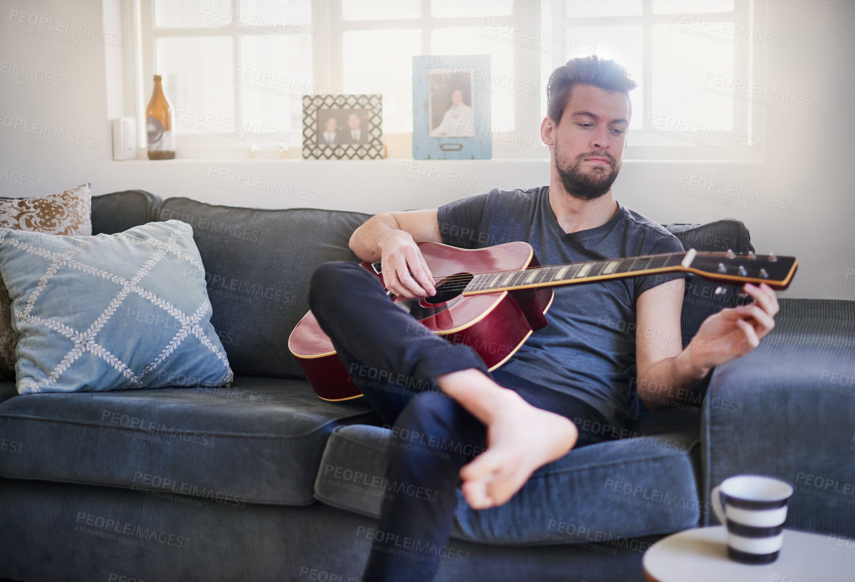 Buy stock photo Cropped shot of a handsome young man playing a guitar at home