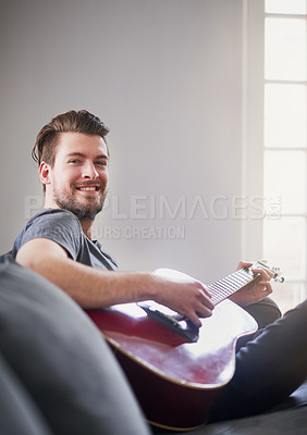 Buy stock photo Portrait of a handsome young man playing a guitar at home
