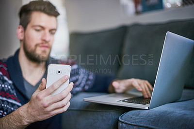Buy stock photo Man, cellphone and laptop at home, couch and social media, website or technology. Multi tasking, text message and typing in internet, mobile and living room or male person, remote work and freelancer