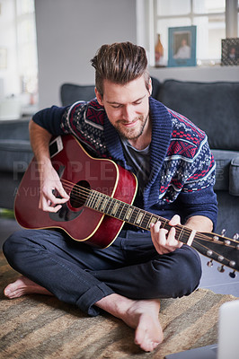 Buy stock photo Shot of a handsome young man playing a guitar at home