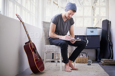 Buy stock photo Shot of a handsome young man writing his own song at home