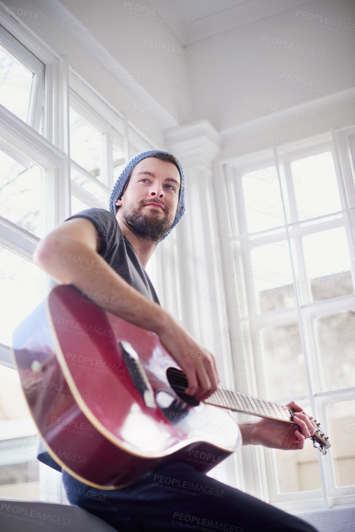 Buy stock photo Cropped shot of a handsome young man playing a guitar at home