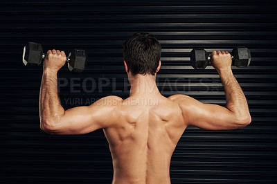 Buy stock photo Rearview shot of a shirtless and well built man lifting dumbbells warming up against a dark background