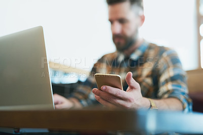 Buy stock photo Shot of a young man using his cellphone and laptop while sitting in a cafe