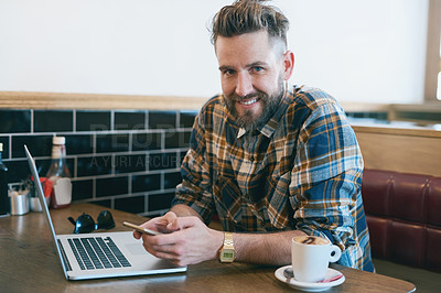 Buy stock photo Portrait of a young man using his cellphone and laptop while sitting in a cafe