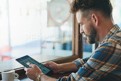 Buy stock photo Shot of a young man using his tablet while sitting by the window in a cafe