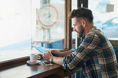 Buy stock photo Shot of a young man using his tablet while sitting by the window in a cafe