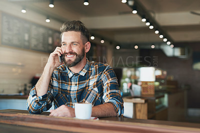 Buy stock photo Shot of a young man talking on his cellphone while sitting by the window in a cafe