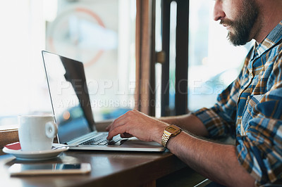 Buy stock photo Shot of a young man using his laptop while sitting by the window in a cafe