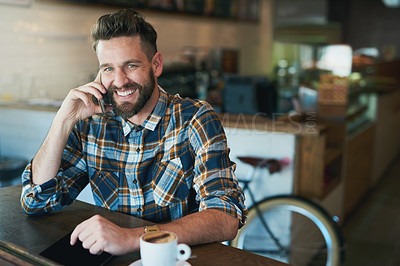 Buy stock photo Shot of a young man talking on his cellphone while sitting by the window in a cafe