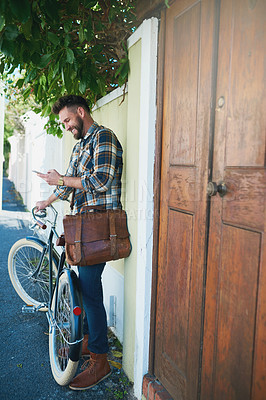 Buy stock photo Shot of a young man using his cellphone while standing outside with his bicycle