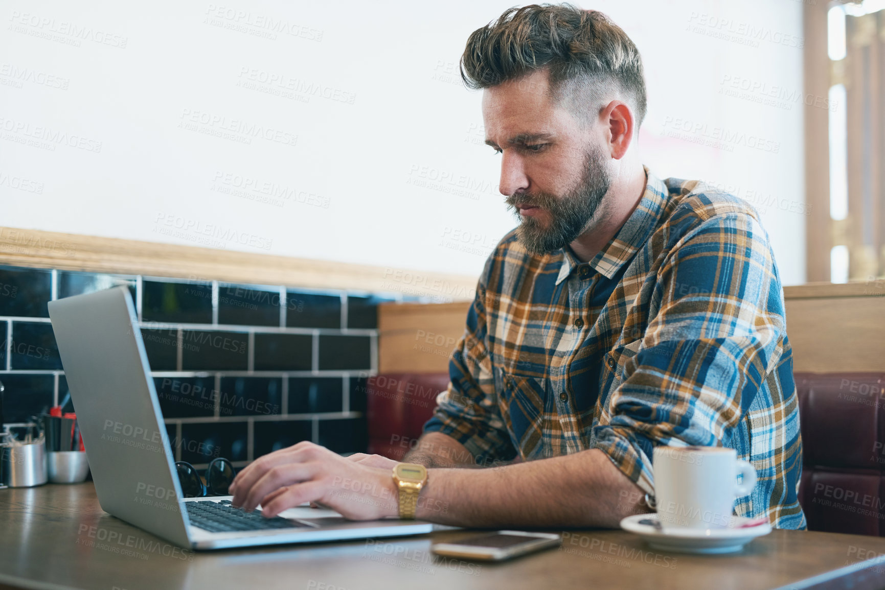 Buy stock photo Shot of a young man using his laptop while sitting in a cafe