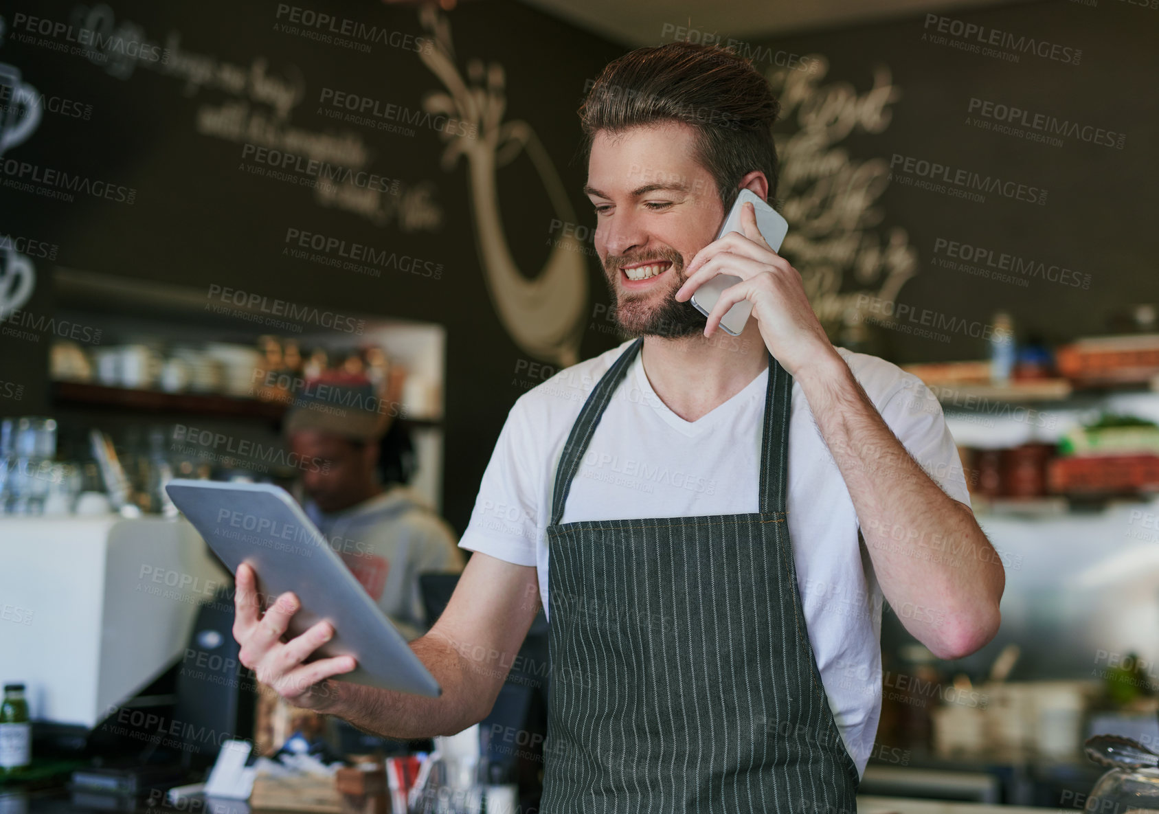 Buy stock photo Shot of a young barista taking orders via cellphone and logging them on his tablet