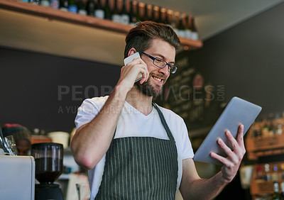 Buy stock photo Shot of a young barista taking orders via cellphone and logging them on his tablet
