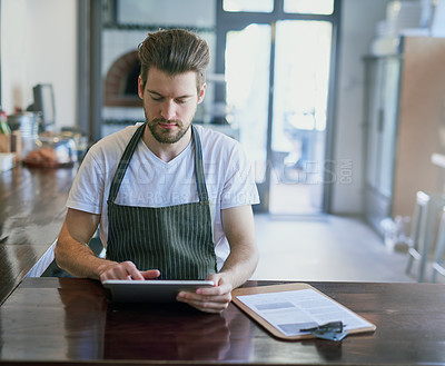 Buy stock photo Cropped shot of a young barista using a tablet in his coffee shop