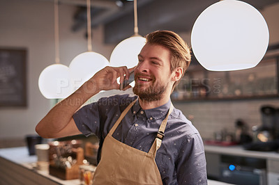 Buy stock photo Shot of a friendly barista talking on his cellphone