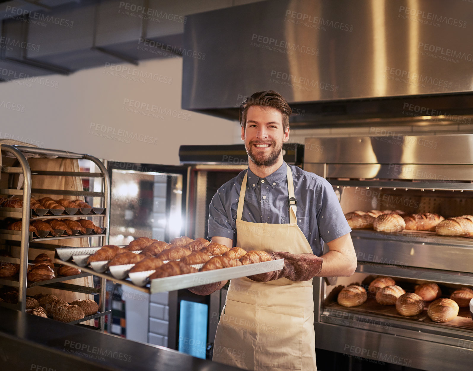 Buy stock photo Cropped shot of a man taking out a fresh batch of croissants to serve to his customers