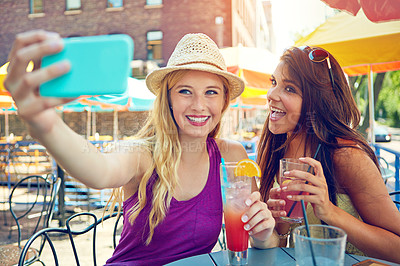 Buy stock photo Shot of two attractive young women taking a selfie while sitting at an outdoor cafe