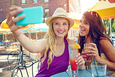 Buy stock photo Shot of two attractive young women taking a selfie while sitting at an outdoor cafe