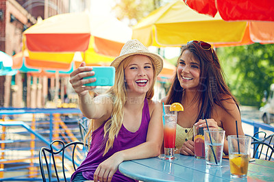 Buy stock photo Shot of two attractive young women taking a selfie while sitting at an outdoor cafe