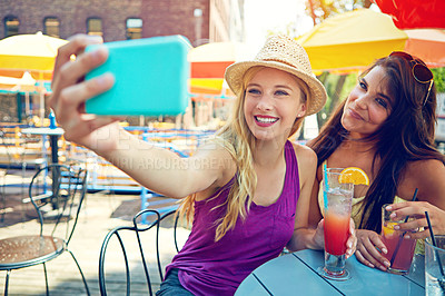 Buy stock photo Shot of two attractive young women taking a selfie while sitting at an outdoor cafe