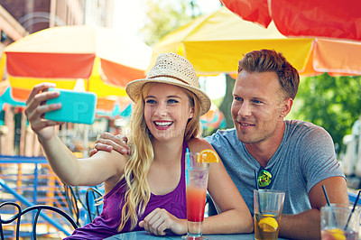 Buy stock photo Shot of a young couple taking a selfie while sitting at an outdoor cafe