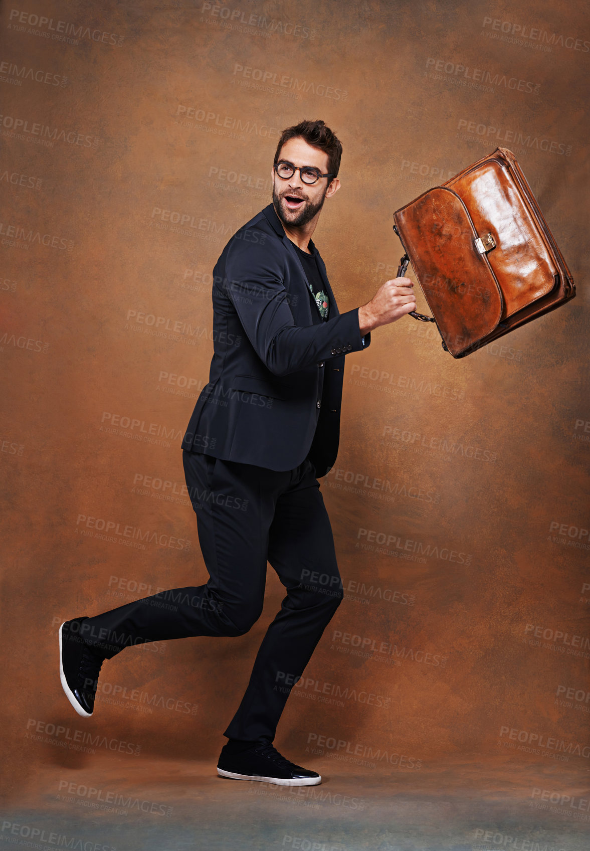 Buy stock photo Briefcase, fashion and man in studio with glasses for trendy, edgy and stylish outfit with confidence. Goofy, satchel and person with blazer for classy style running for comedy by brown background.