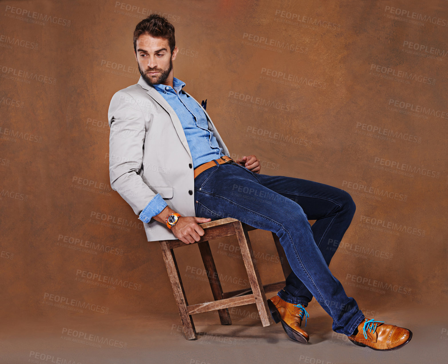 Buy stock photo Fashion, serious and man in studio with trendy, stylish and classy suit on chair with confidence. Model, handsome and male person with elegant style for outfit and accessory by brown background.