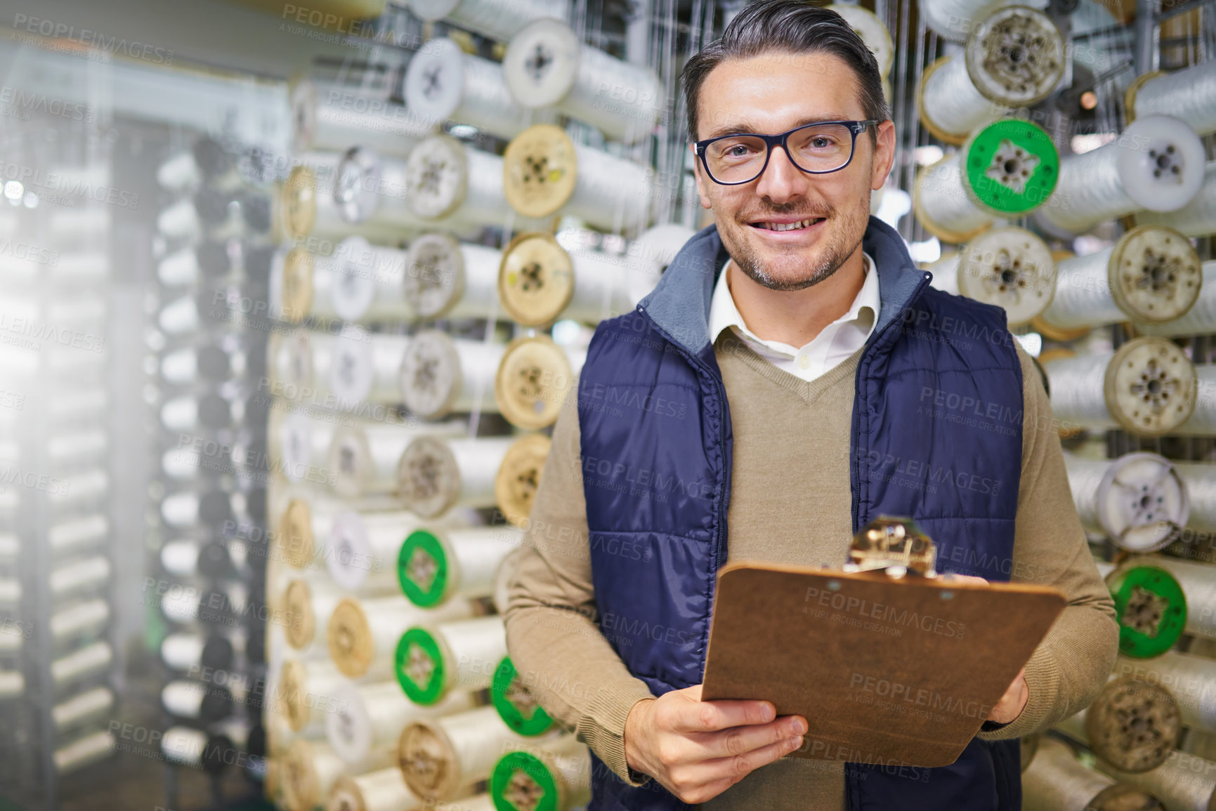 Buy stock photo Portrait of a manager holding a clipboard while standing in front of wire spools on the factory floor