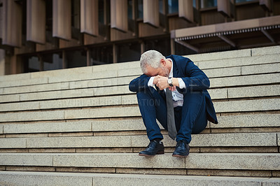 Buy stock photo Shot of a dejected businessman sitting on the stairs outside his office with his head in his hands