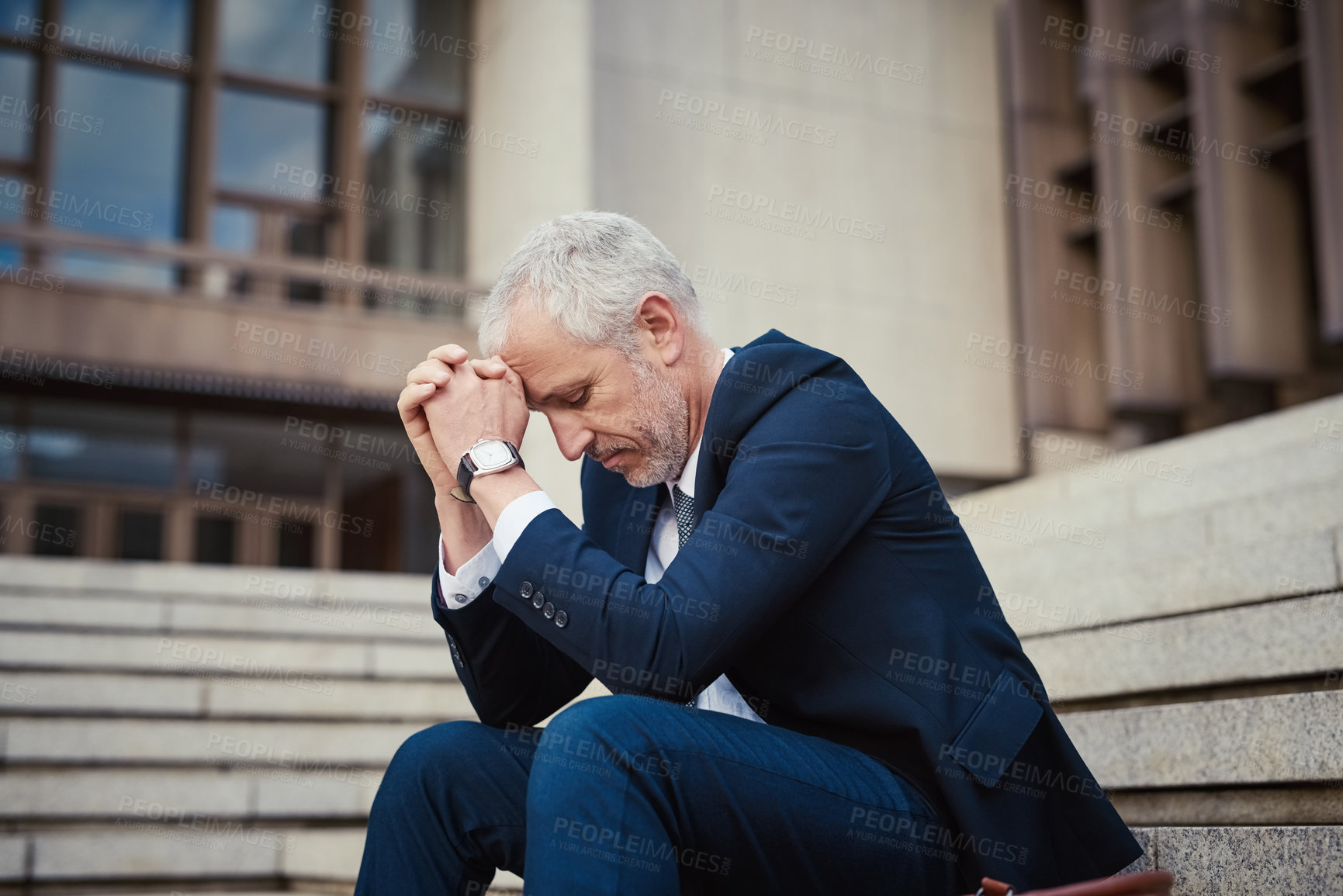 Buy stock photo Shot of a dejected businessman sitting on the stairs outside his office with his head in his hands