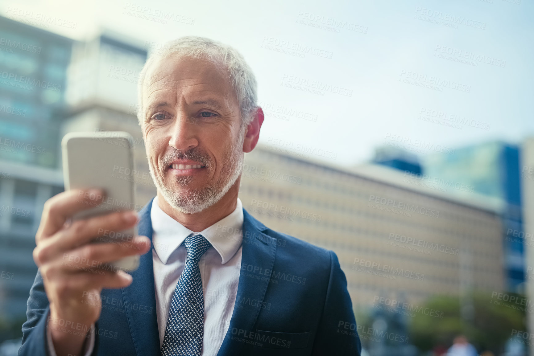 Buy stock photo Shot of a confident businessman using his cellphone while standing outside his office building