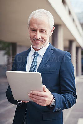 Buy stock photo Shot of a confident businessman using his tablet while standing outside his office building