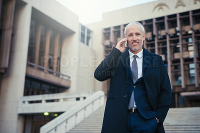 Buy stock photo Shot of a businessman answering his phone while standing outside his office in the city