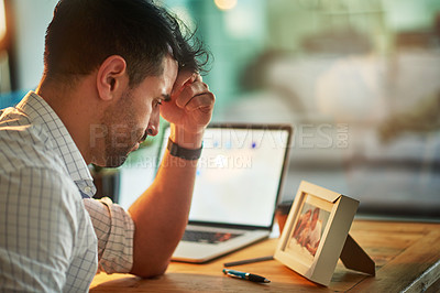 Buy stock photo Shot of a worried businessman looking at a picture of his family while sitting at his desk