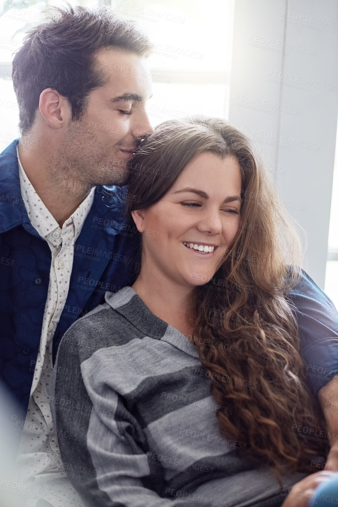 Buy stock photo Shot of a young man smelling his girlfriend's hair while they relax at home together
