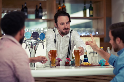 Buy stock photo Shot of a friendly barman serving beer to two customers at his bar