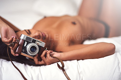 Buy stock photo Shot of a beautiful naked young woman lying in bed holding a vintage camera