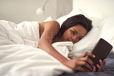 Buy stock photo Shot of a young woman taking a selfie while lying in bed covered in sheets