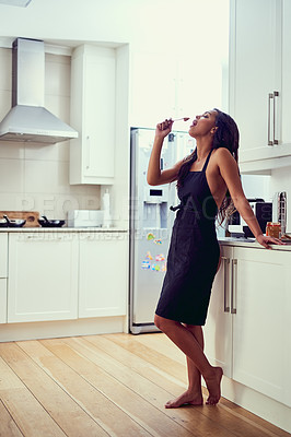 Buy stock photo Shot of a beautiful young woman sensually eating peanut butter from a spoon while standing her kitchen in her underwear and an apron