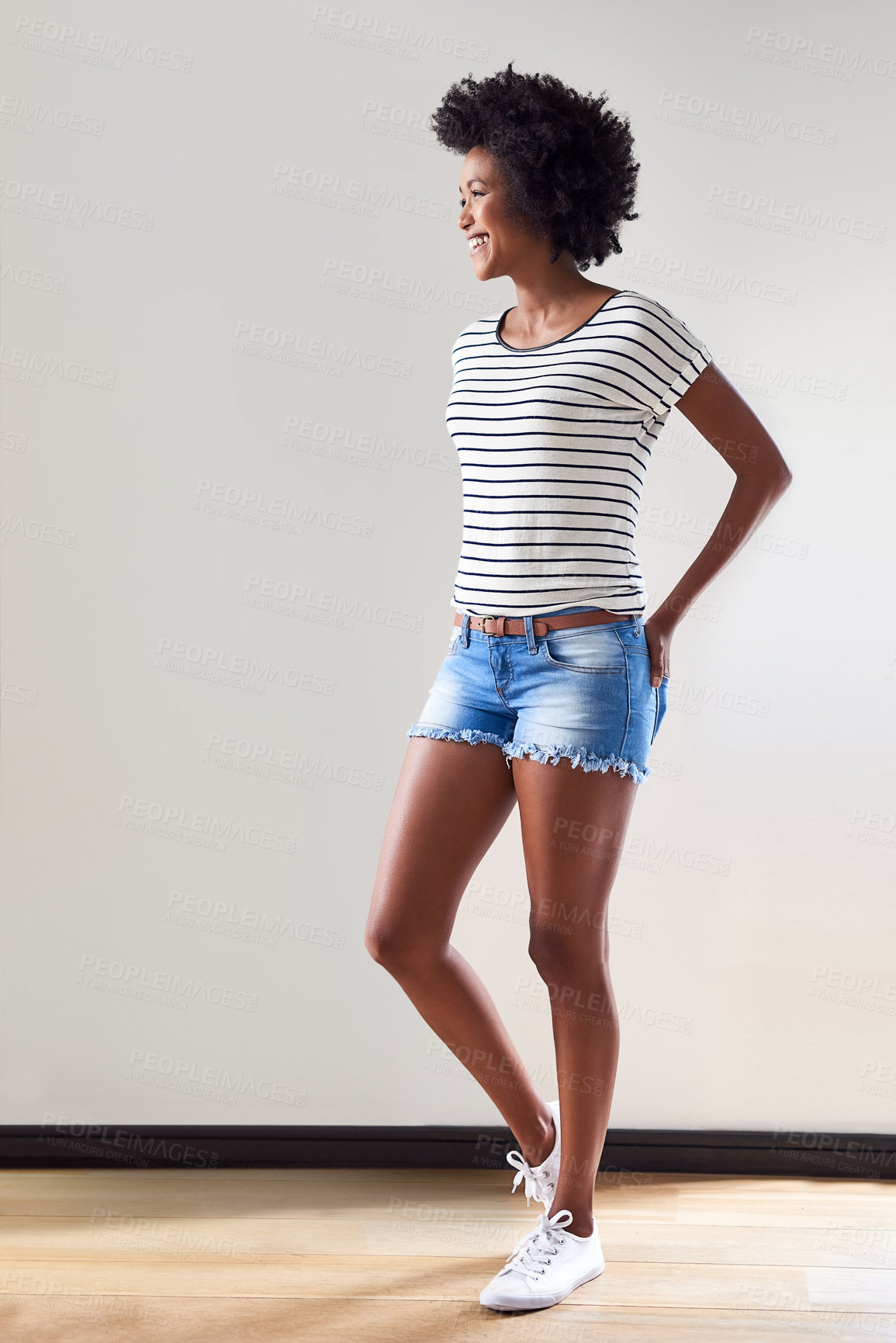Buy stock photo Shot of an attractive and happy young woman wearing a striped sweater and denim shorts indoors